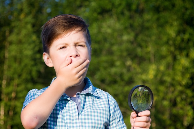 Shocked boy with magnifying glass in summer