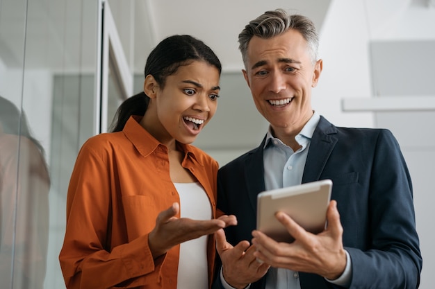 Shocked business people using digital  tablet looking at screen, reading news working in office