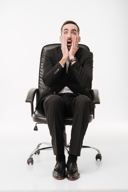 Shocked businessman over white wall sitting on chair.