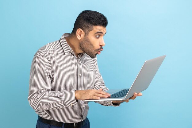 Shocked businessman with beard looks at laptop display with opened mouth and big eyes system error