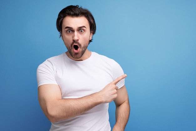 Shocked by surprise brunette young man in a white tshirt with biceps on a studio background with