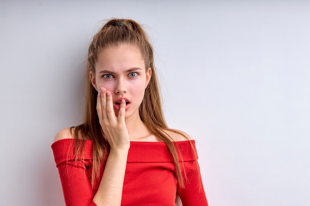 Shocked caucasian female opens mouth widely from surprisement feels troubled and concerned wearing r...