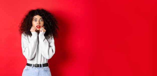 Shocked caucasian woman with curly hairstyle looking at something impressive gasping amazed checking