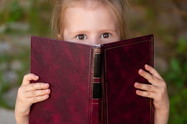 Foto bambino scioccato che tiene il libro nelle sue mani guardando la fotocamera emozioni del libro di lettura della scolaretta