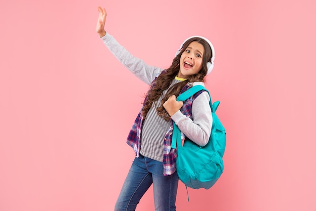 ショックを受けた子供はヘッドフォンで音楽を聴き、ピンクの背景、現代の生活にバックパックを運びます。