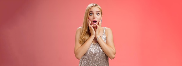 Shocked concerned stunned young european blond woman in silver dres drop jaw widen eyes stunned