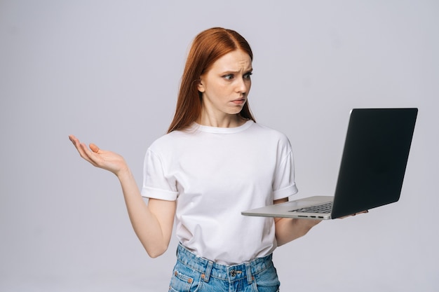 Shocked confused young business woman holding keeping opened laptop computer and looking at screen