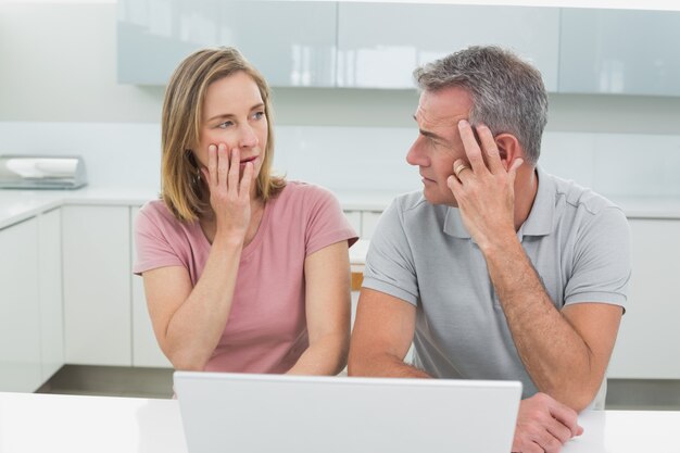 Shocked couple using laptop in kitchen