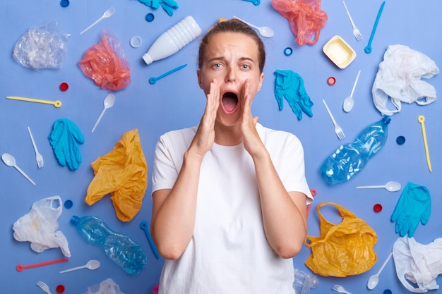 Shocked dark haired woman screaming loud keeps hands near mouth looks at camera realizes problem of pollution wearing casual clothes worries about nature disaster Ecology volunteering