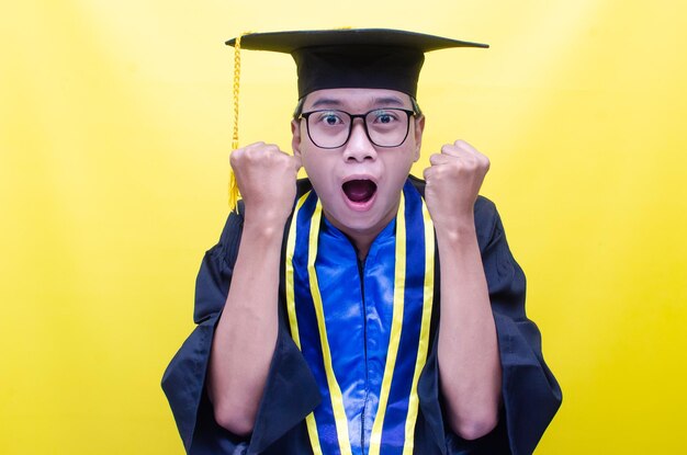 shocked and ecstatic Asian man in graduation cap and gown raising fist celebrating his graduation