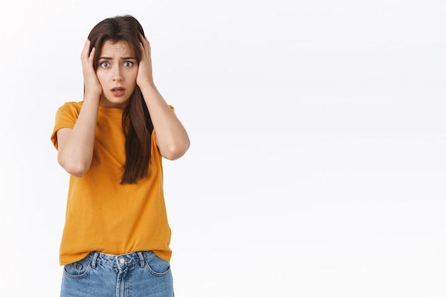 Shocked, embarrassed young woman remember humiliating thing she did, hold hands on head, gasping and open mouth look troubled, uneasy feeling scared, standing worried white background