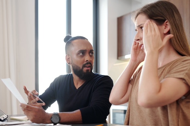 Photo shocked emotional man with bill in hand looking at wife who forgot to pay monthly mortgage payment