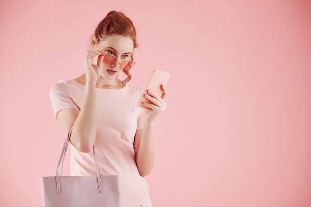 Shocked emotional young woman taking off glasses and reading
notification or text message on smartphone