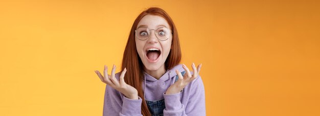 Photo shocked excited overwhelmed young screaming happy redhead girl wearing glasses winning hear