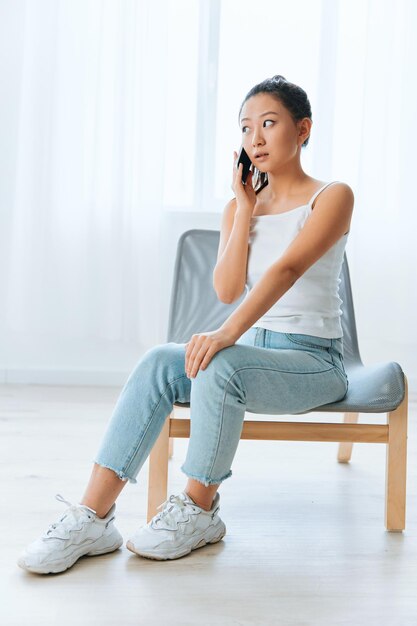 Shocked excited tanned lovely young asian woman get surprised\
information in call using phone at home interior living room\
distance communication social media concept cool offer banner wide\
angle