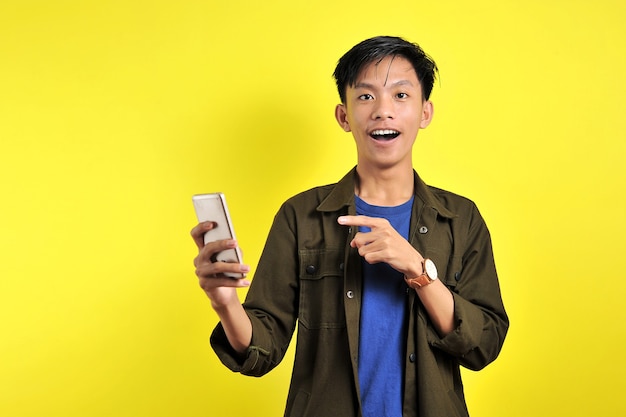 Shocked face of Asian man in white shirt looking at phone screen on yellow background.