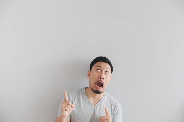 Shocked face of man in grey t-shirt with hand point on empty space.