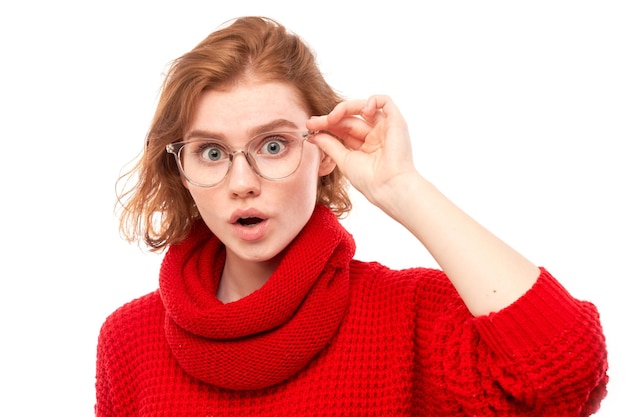 Shocked face red-haired girl in glasses looks surprised with open mouth on white studio background