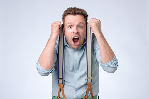 Shocked face of young european man in blue shirt and suspenders