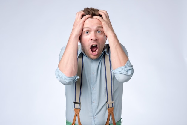 Shocked face of young european man in blue shirt and suspenders