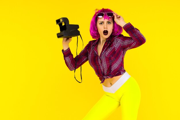 Shocked girl portrait with camera on yellow background