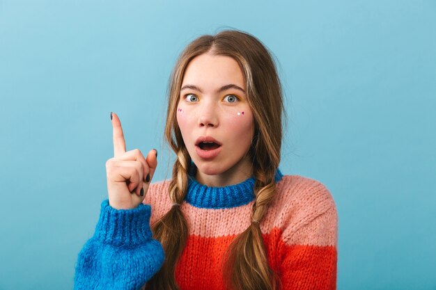 Shocked girl wearing sweater standing isolated, pointing up