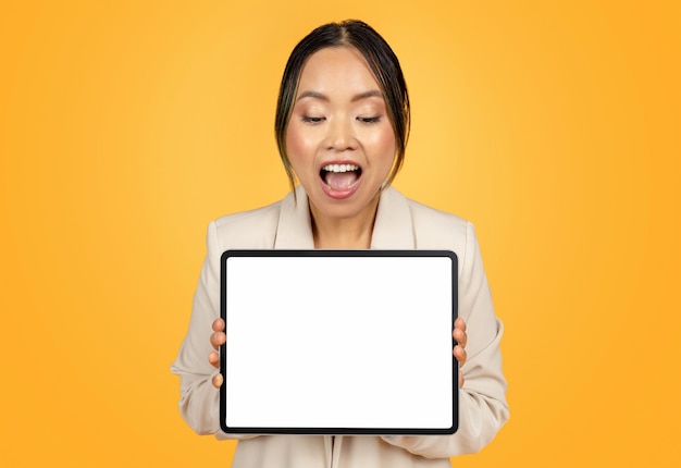 Shocked glad millennial japanese lady in suit show tablet with empty screen