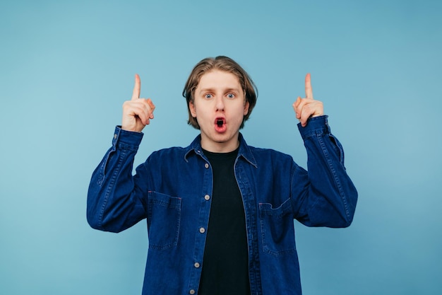 Shocked guy in a blue shirt stands on a blue background with a shocked face looking at the camera