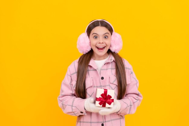 Shocked happy kid in winter earmuffs with box teen girl in mittens hold present