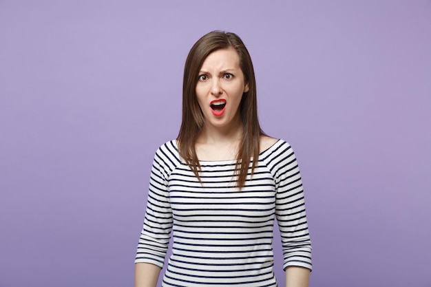 Shocked irritated young woman girl in casual striped clothes posing isolated on violet purple background studio portrait. People lifestyle concept. Mock up copy space. Swearing, keeping mouth open.