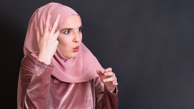 Shocked islamic woman standing against black backdrop