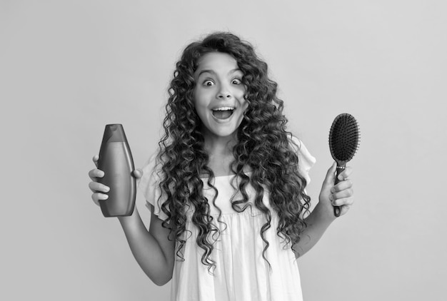 Shocked kid curly hair hold comb and shampoo bottle teen beauty hairstyle