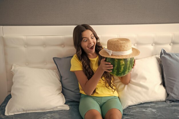 Shocked kid holding fresh ripe water melon fruit in summer straw hat food