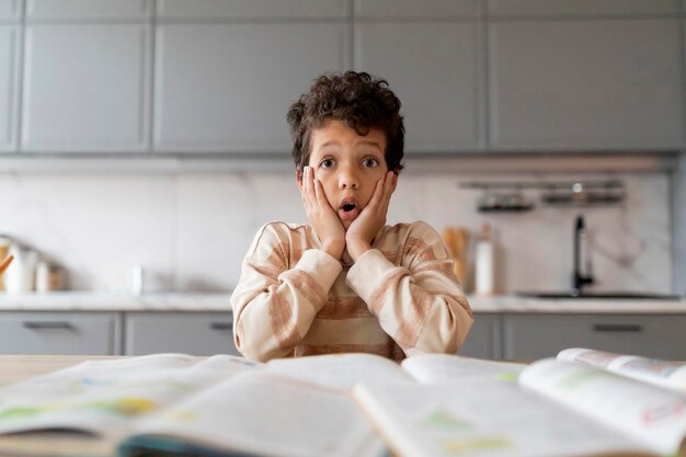 Photo shocked little black boy looking at workbooks and touching face