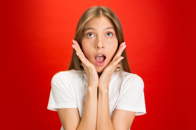 Shocked looking up. Portrait of young caucasian woman on red studio wall