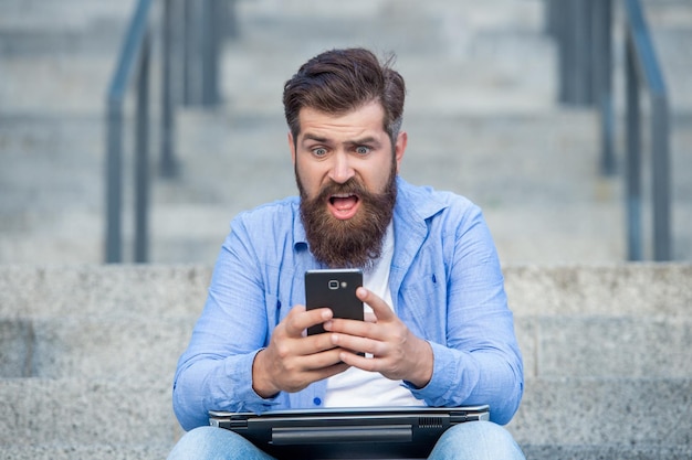 屋外の階段に座って携帯電話の賭けの結果をチェックするショックを受けた男