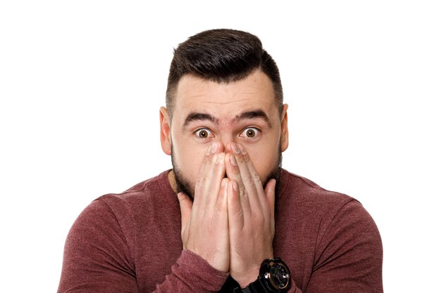 Shocked man covers his face with his hands on white background.