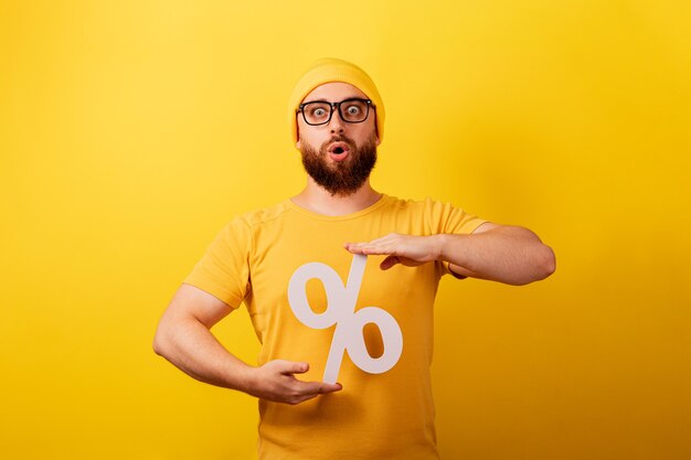 Шокированный мужчина держит знак процента на желтом фоне, скидки с высоким процентом