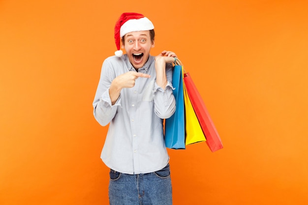 Shocked man holding many bags and pointing fingers on them