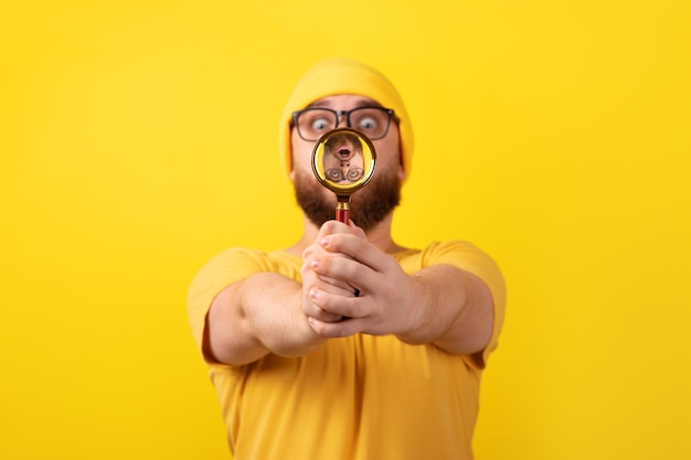 Shocked man looking through magnifier glass over yellow background