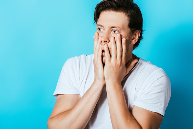 Shocked man with hands near cheeks looking away on blue background