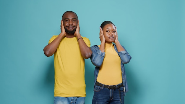 Shocked man and woman covering mouth, eyes and ears in front of camera. Couple in disbelief having expressive reaction with hand, doing gesture to cover face. Worried people with fear.