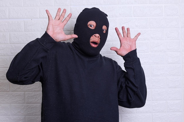 Shocked masked thief with raised arms isolated on white background