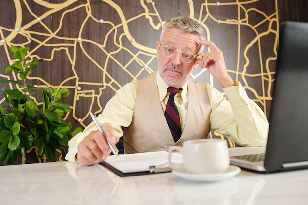 Шокированный зрелый бизнесмен делает широко раскрытые глаза при чтении документа на своем столе