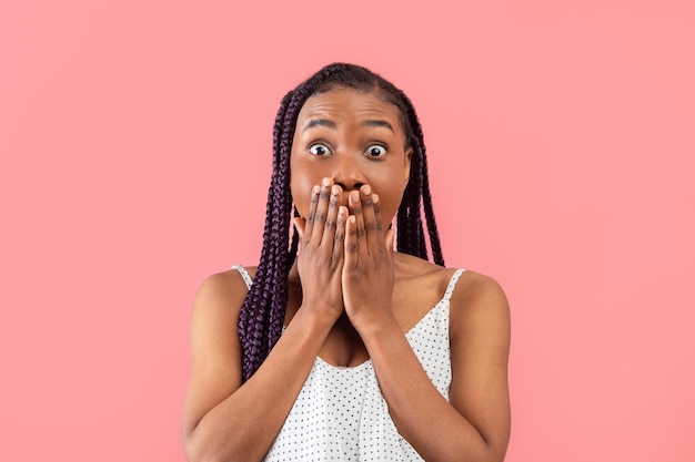 Shocked millennial black woman covering her mouth with hands in terror on pink studio background