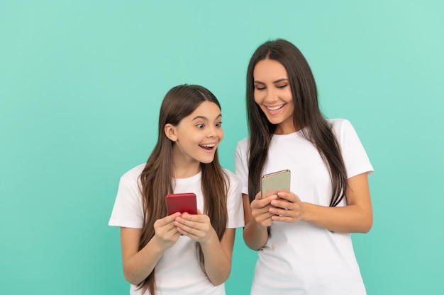 Shocked mother and daughter chatting on smartphone on blue background