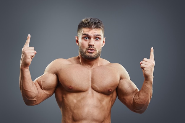 Photo shocked muscular young man pointing upwards