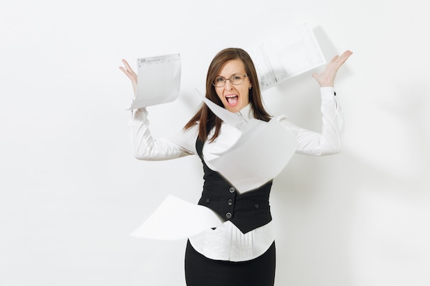 Shocked perplexed stress angry caucasian young business woman in black suit, white shirt, glasses throwing work documents isolated on white wall