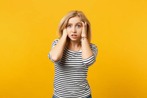 Shocked perplexed young woman in striped clothes looking camera putting hands on head isolated on yellow orange background in studio. people sincere emotions, lifestyle concept. mock up copy space