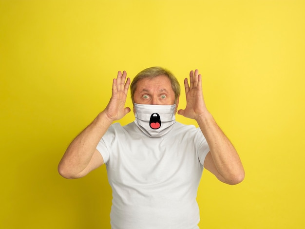 Shocked. Portrait of caucasian senior man with emotion on his protective face mask isolated on studio background. Beautiful male model. Human emotions, facial expression, sales, ad concept.